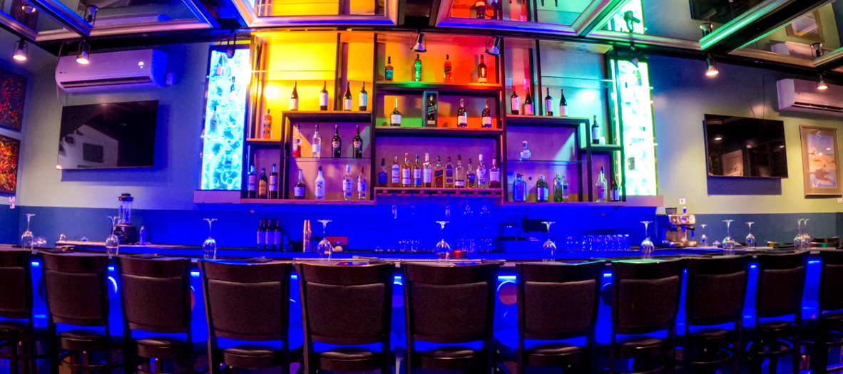 The SeaRock bar glowing at night, colour-lit spirits wall and harbour-blue counter