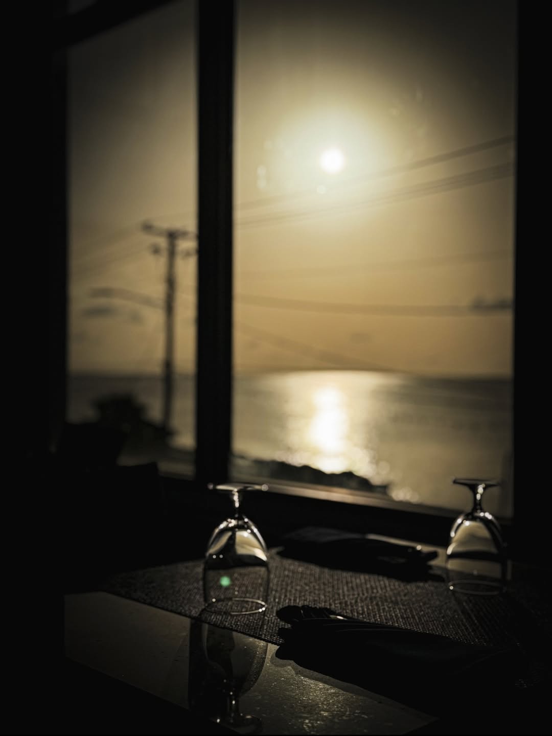 Sunset over George Town harbour through SeaRock's windows, with wine glasses on the table